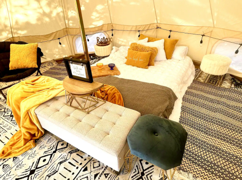 Cozy tent interior with a bed, decorative pillows, a coffee table, and patterned rugs, creating a warm, inviting atmosphere.